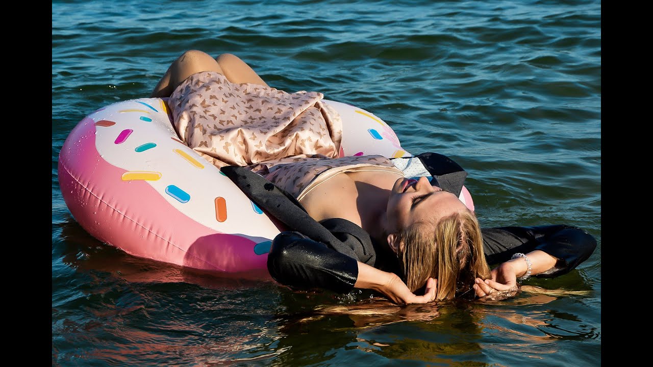 A STUDENT GIRL SWIMS ON AN INFLATABLE CIRCLE AND POSES IN WET CLOTHES ON THE BEACH BY THE SEA