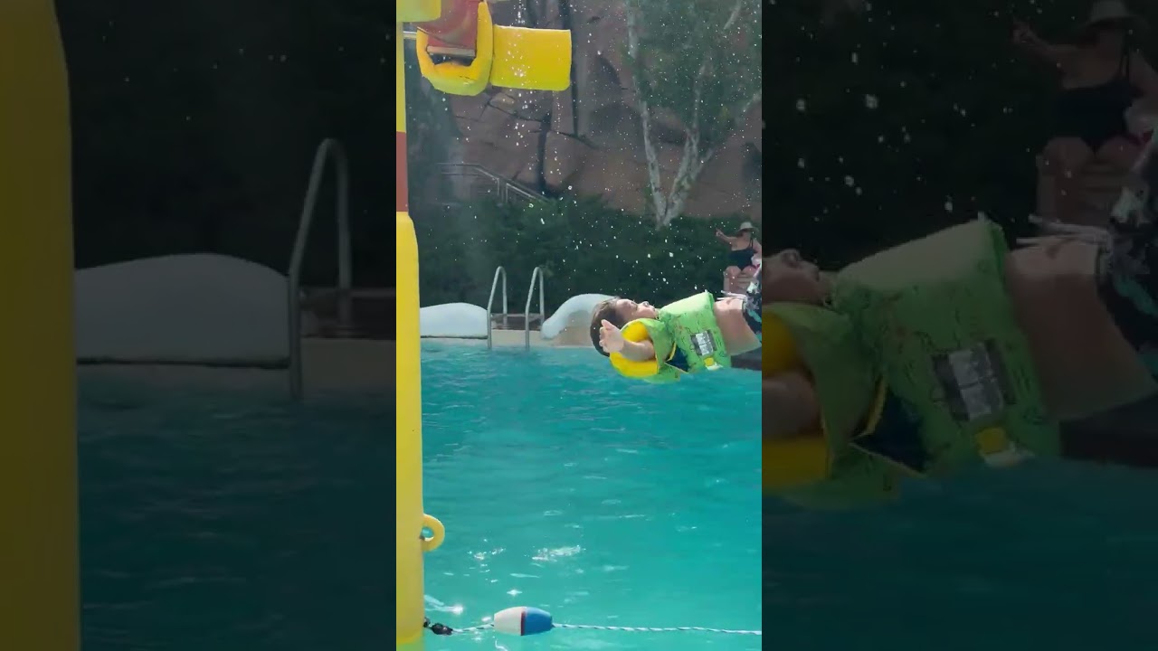 Little boy in life jacket goes on zipline then flips back and lands in water