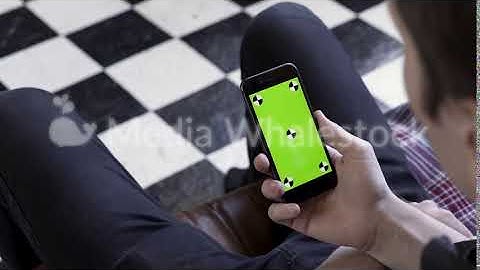 Male holding black smart phone with green screen and tracking marks on black and white checkered