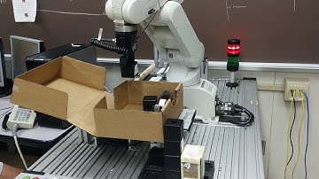 Industrial robot stacking a box and closing the lid.