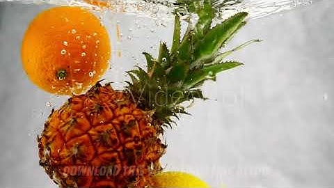 Pineapple, orange and lemon falls into the water with splashes and bubbles in slow motion.