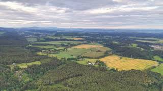 Aerial panorama over patchwork fields, dense forests, scattered farmsteads, winding roads, and