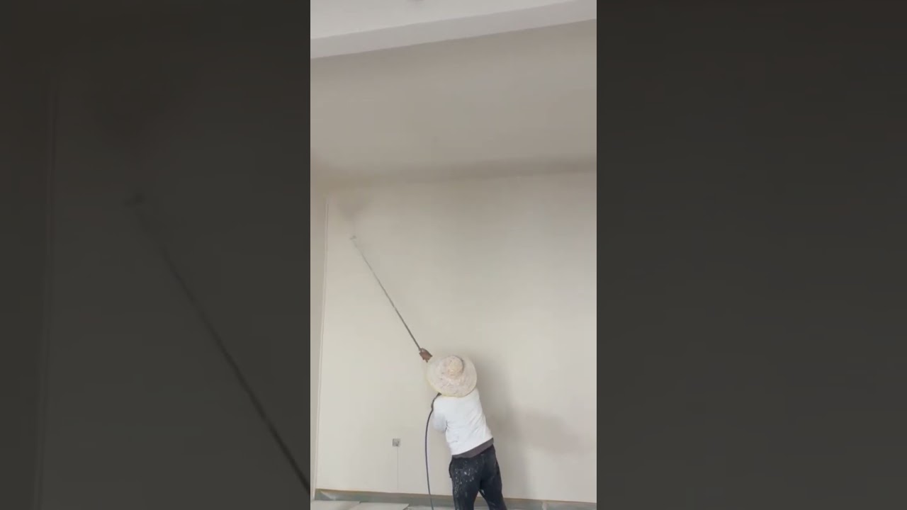 spraying liquid white paint on a large interior wall surface using a professional sprayer machine