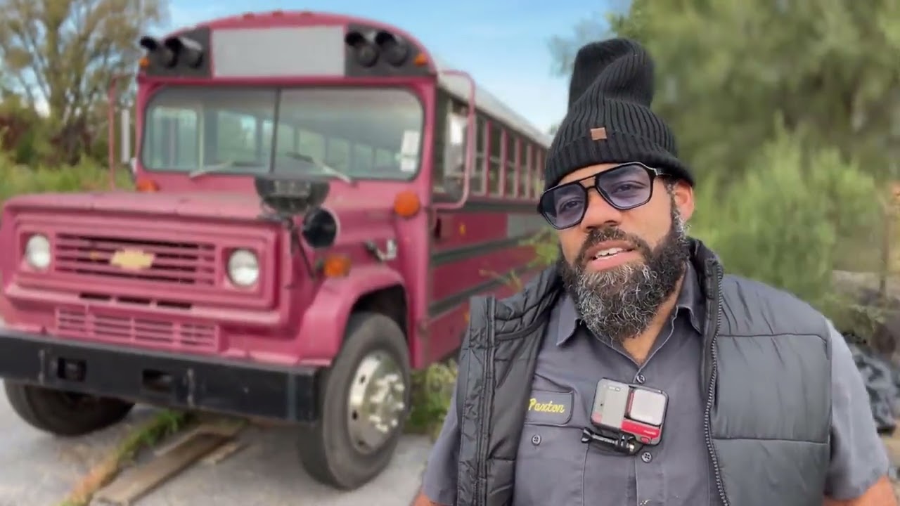 A bearded man with a winter hat and coat in front of a pink school bus