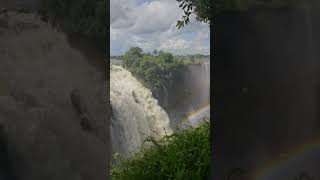 Majestic Victoria Falls cascading down basalt cliffs on Zambezi River with rainbow emerging from