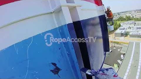 Rope access technician painting a commercial building with paintbrush and paint roller