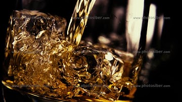 Slow motion pour bourbon into a glass of ice