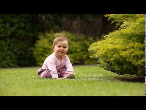 Beautiful happy little baby girl sitting on a green meadow near the bush.