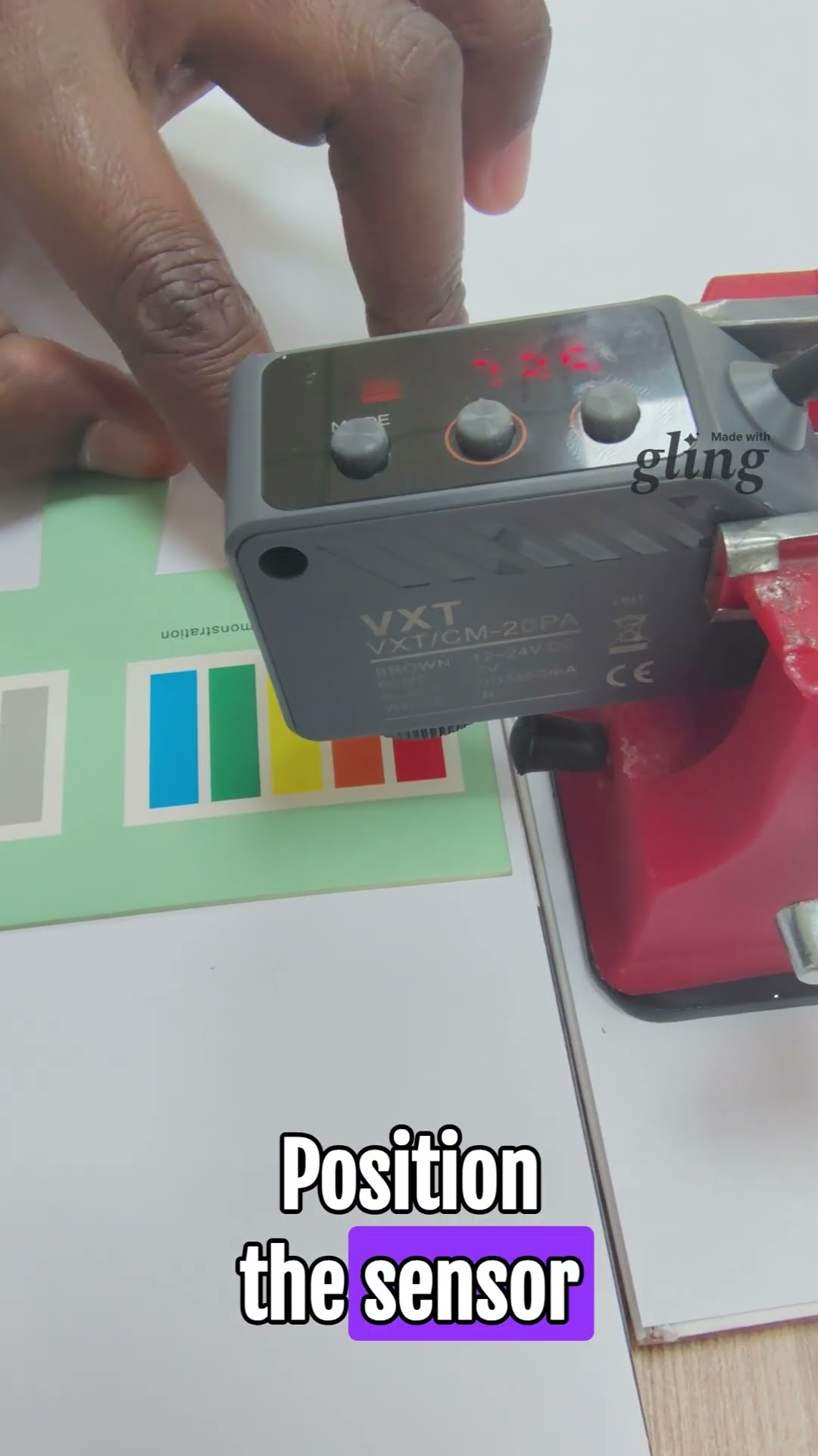 VXT/CM-20PA colour mark sensor held above a printed colour swatch card, red digital display lit