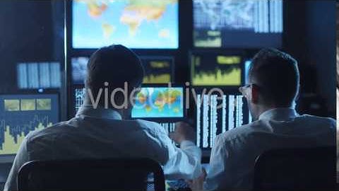 Two Employees are Working on Computers in a Weather forecast Centre Filled with Display Screens |