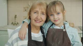 Portrait of grandmother and granddaughter in aprons smiling looking at camera in kitchen