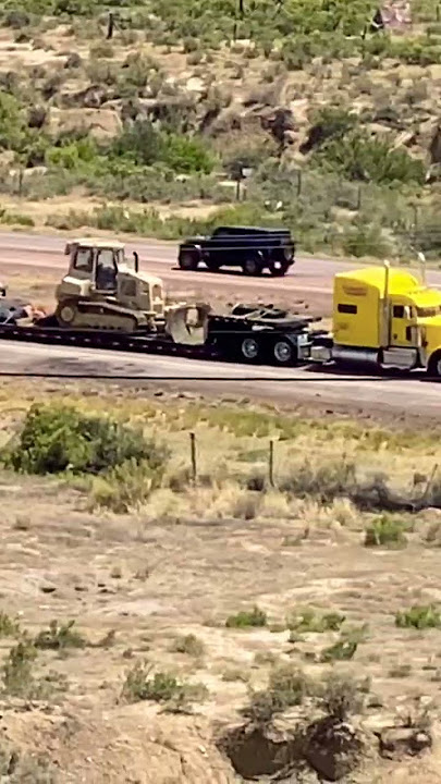 Military construction bulldozer vehicle being transported on yellow semi trailer