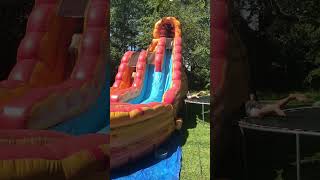 Guy attempts to backflip from trampoline onto bounce house castle slide and lands on his back