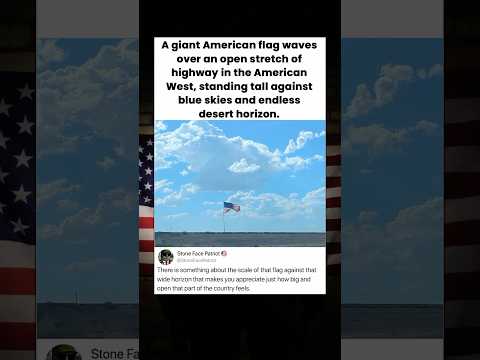 A giant American flag waves over an open stretch of highway in the American West, standing
