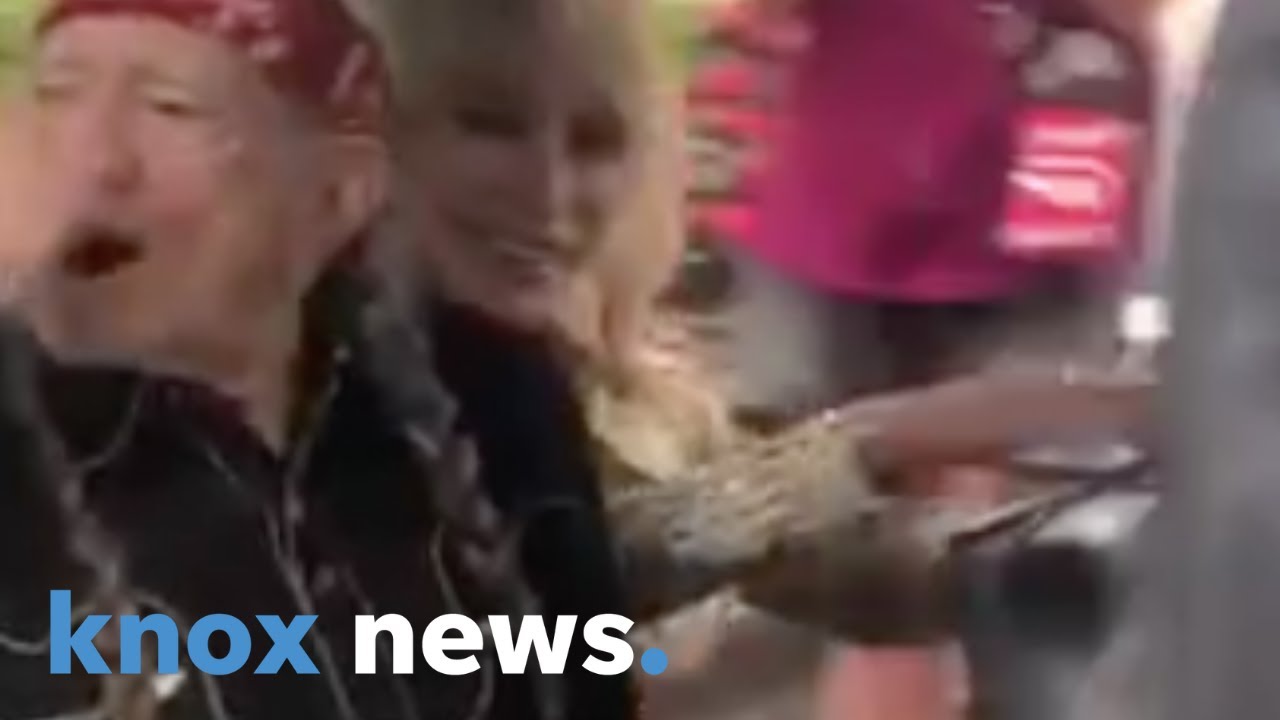 Dolly Parton and Willie Nelson ride a golf cart and wave to fans at