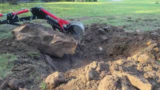 Harbor Freight towable trencher/backhoe dragging a boulder out of the ground.
