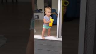 Little girl walks out of sliding door onto deck with her sippy cup then slips on water