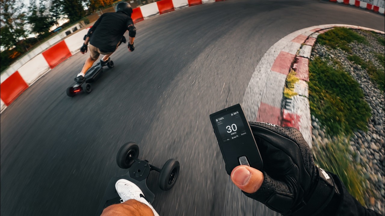 Due rider su longboard elettrici ONSRA in una curva di pista, una mano tiene un telecomando, anteprima del video