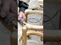 A woodworker is using a rotary tool to sand a wooden chair frame