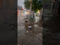 Debris Floats Down Queens Street as Man Wades Through Floodwaters