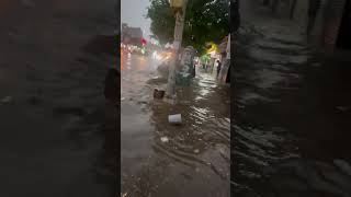 Debris Floats Down Queens Street as Man Wades Through Floodwaters