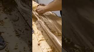 carefully smoothing a large decorative wooden board by hand to create detailed wavy pattern surface