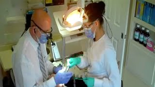 Doctor And Assistant Passing Instruments During OverTheHead Delivery Of FourHanded Dentistry