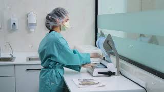 Woman technician cuts off packaging for dental tools for further disinfection