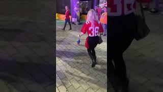 Woman in red jersey holding beer kicks football at game at the fair and ball hits lady on chest
