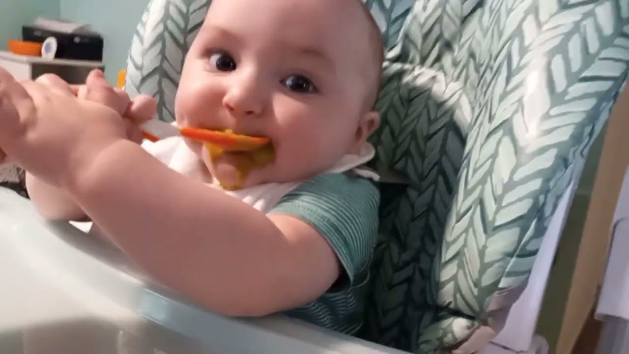 baby eating peas for dinny and watching his cat act foolish
