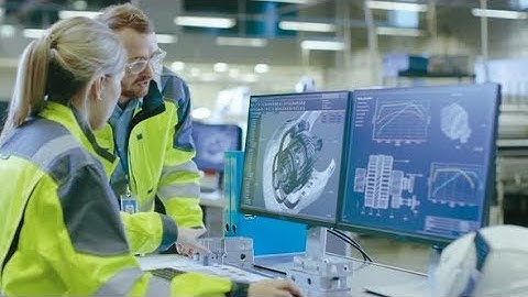 At the Factory: Male Mechanical Engineer Holds Component while Female Chief Engineer Work on PC |