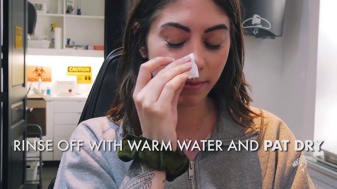 A person carefully cleaning their new nose piercing with saline solution as part of the aftercare process.