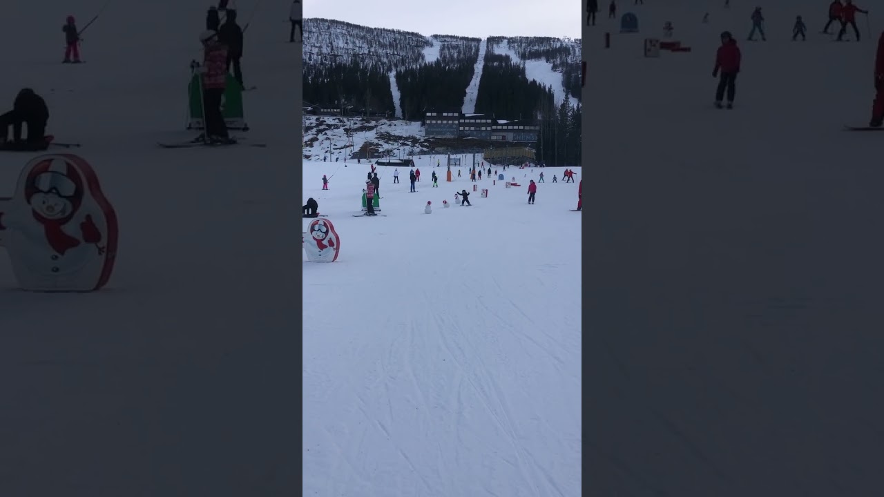 Boy on skis rides down slop then crashes into miniature snow man and falls forward