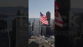 US flag waving in wind on top of building above city. Modern downtown San Francisco, California, USA