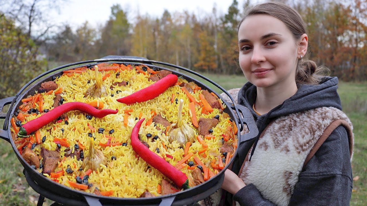 Ukrainian woman cooks tradition Pilaf on an open fire in the village