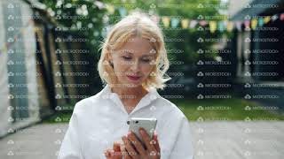 Beautiful mature woman using smartphone touching screen outdoors