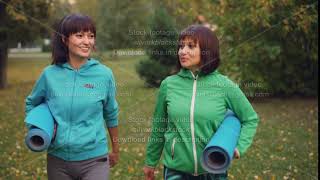 Dolly Shot Of Good-Looking Sportswomen Talking, Smiling And Holding Yoga Mats Walking In Park On