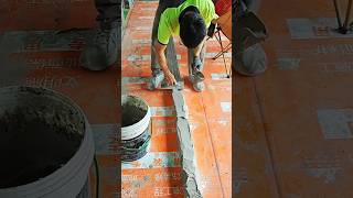Worker smooths wet cement along floor edge carefully.
