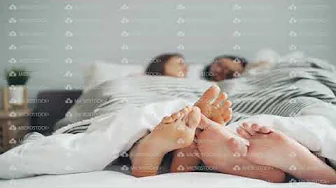 Male and female feet touching in bed couple talking lying together under blanket