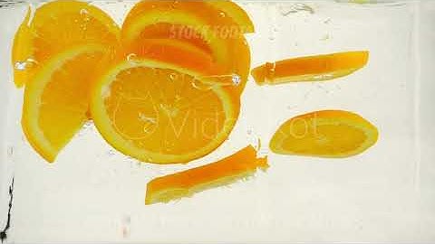 Juicy orange slices fall into water with splashes and bubbles, slow motion close-up