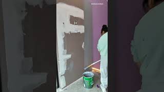applying grey wall paint using a long extension pole paint roller tool over a white plaster wall