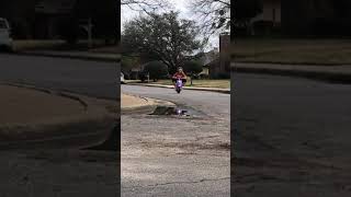 Little girl rides purple electric Moped on street then wobbles and falls into puddle near gutter