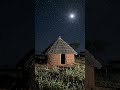 Wide shot of a lonely African hut at night under moonlight.