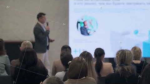 Presenter speaks to audience during conference with blurred proj