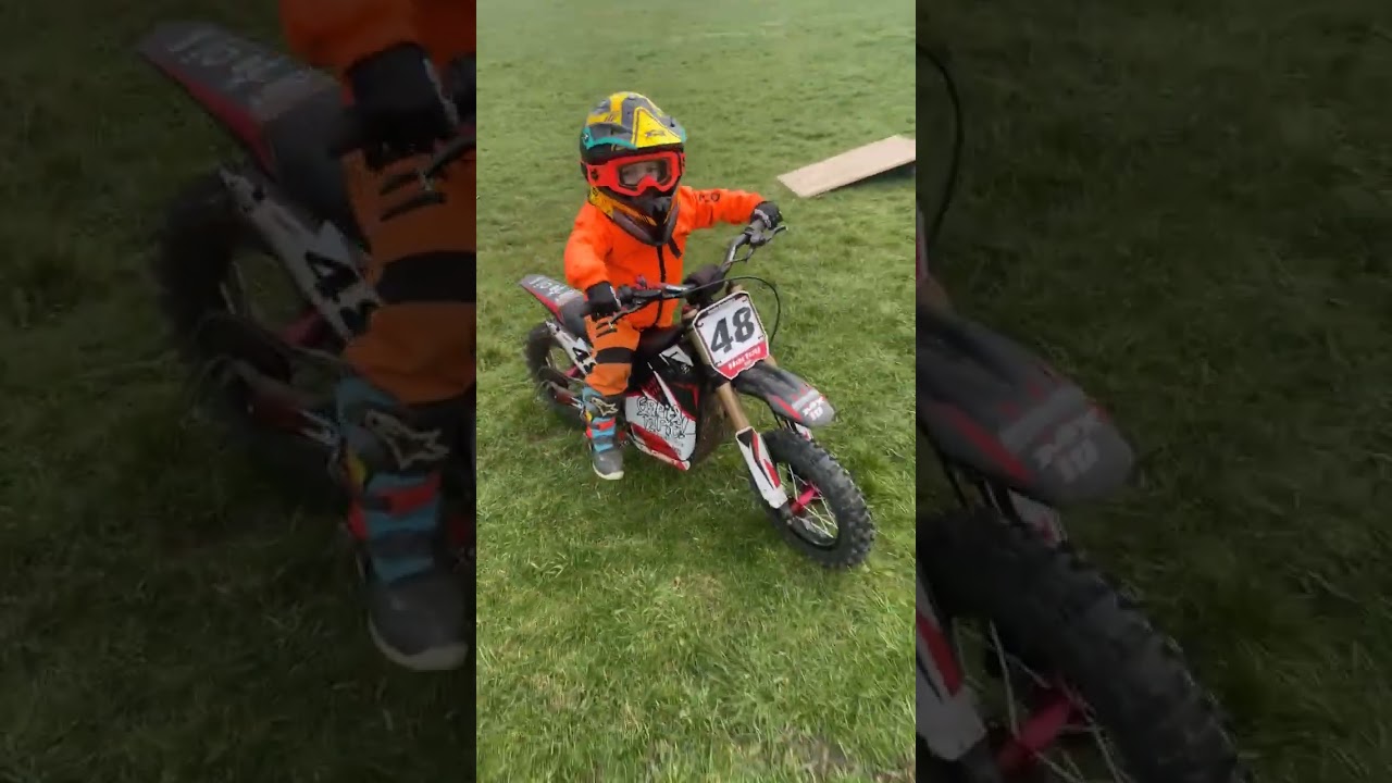Boy in full face helmet does wheelie on dirt bike and falls back on grass