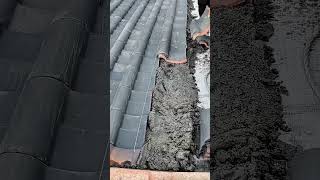 Worker lays gray roof tiles over wet mortar.