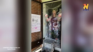 Teacher hugs students through homemade plastic barrier at front door