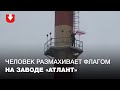 Человек размахивает бело-красно-белым флагом на трубе завода "Атлант" в Минске 28 октября