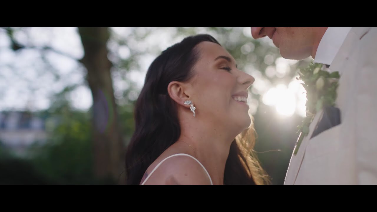 Bride smiles up at the groom in warm backlight, her pearl earrings catching the sun in a garden
