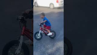 Little boy rides bike in parking lot with no hands then falls off and faceplants